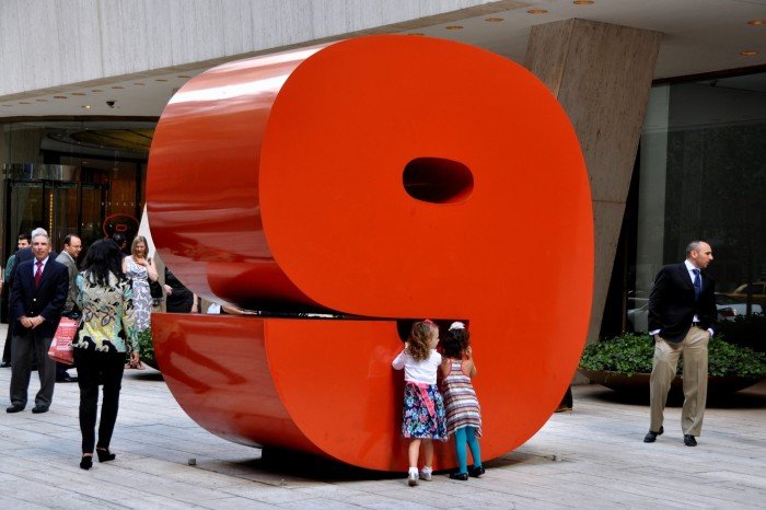 Two young girls play next to a large red sculpture of the number nine outside the 9 West 57th Street office building in Manhattan.