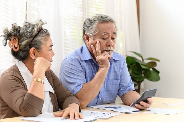A visibly concerned couple examining bills and financial statements while seated at a table in their home.