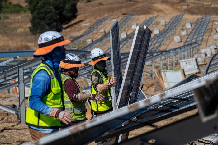 Workers in safety gear install solar panels on metal frames at the Phillips 66 Rodeo Renewable Energy Complex construction site.